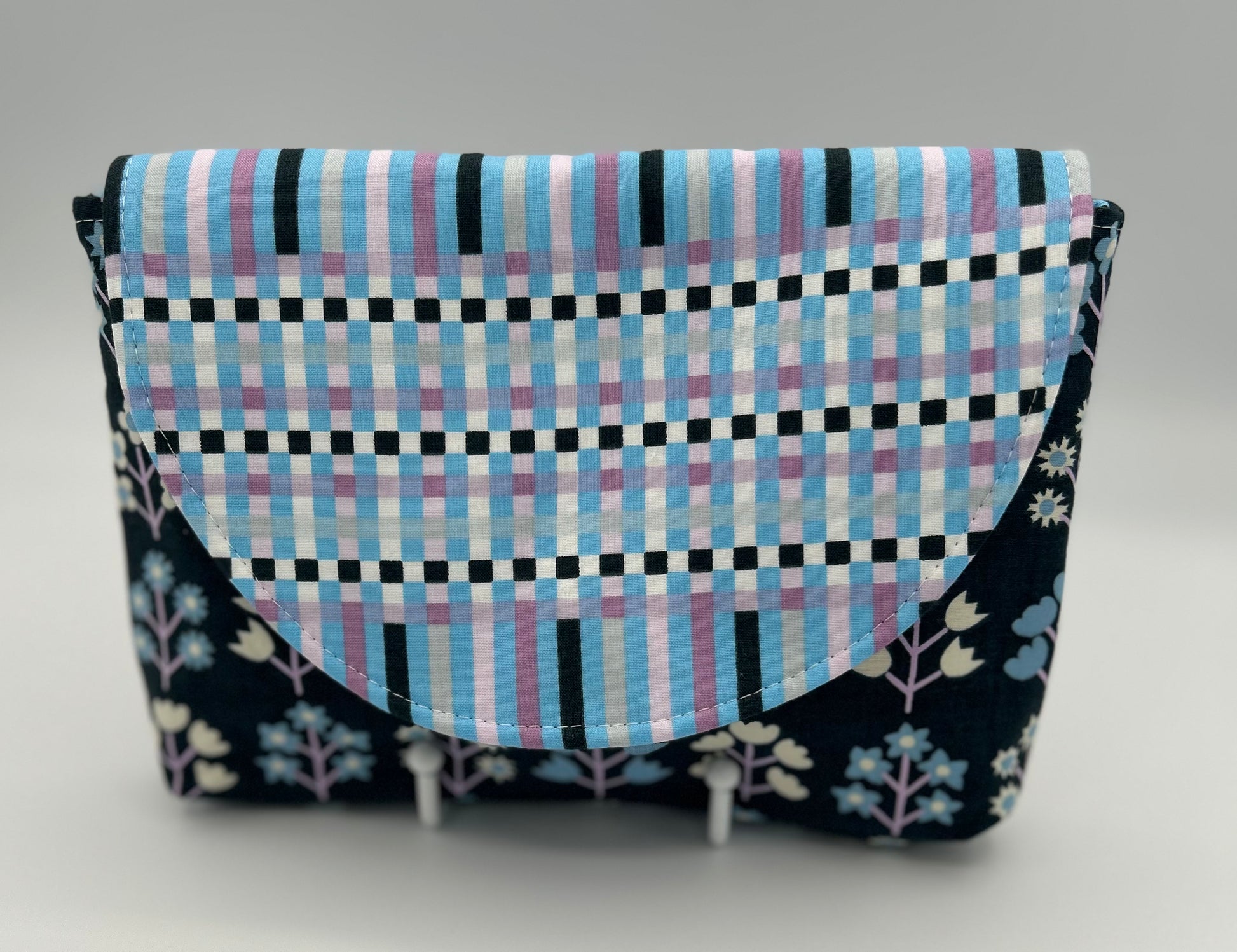 Fabric pouch with checkered pattern and floral accents on a gray background